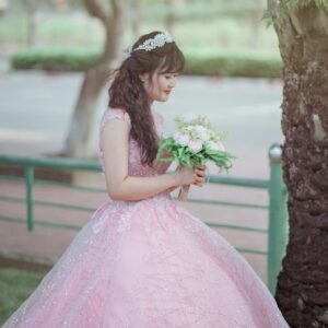A beautiful bride in a pink gown with a bouquet, captured in a serene park setting.