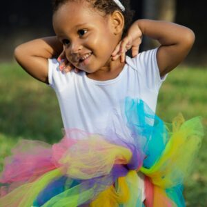 Charming young girl in a vibrant tutu smiling in a sunny outdoor setting.