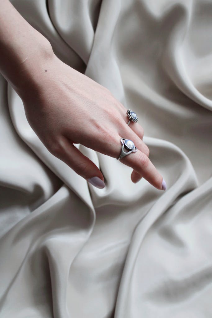 Close-up of a hand wearing silver rings delicately placed on luxurious draped fabric.