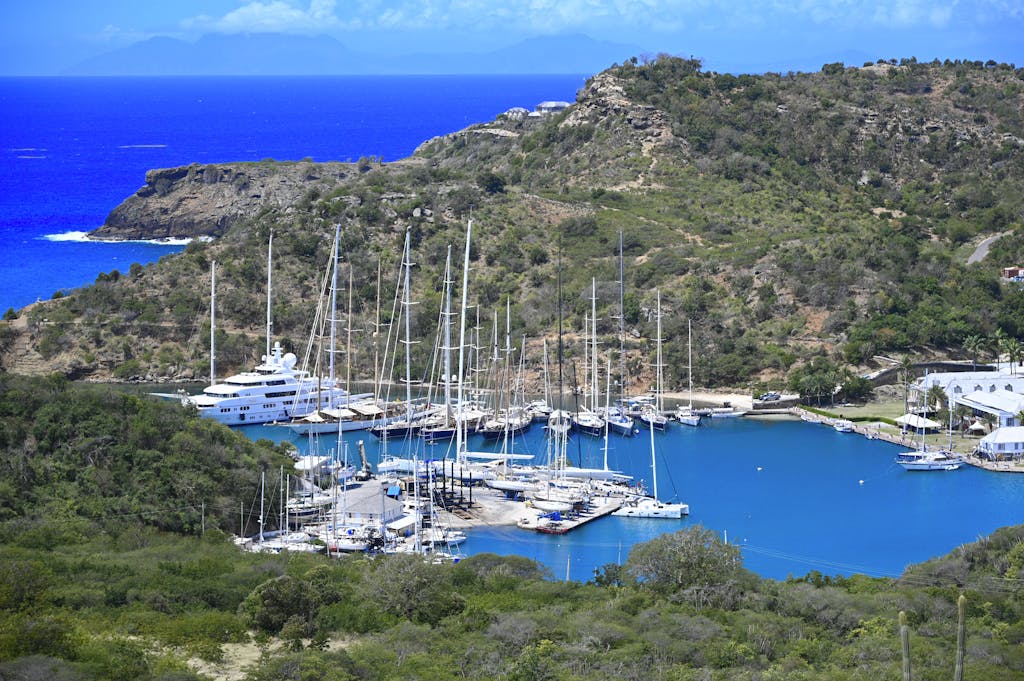 Stunning aerial view of a serene harbor with moored yachts, surrounded by lush hills and vibrant blue water.